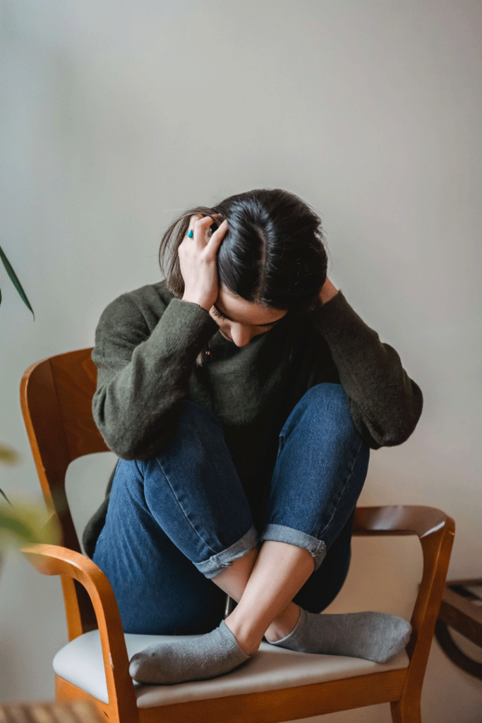 Lady sitting on Chair with crossed legs and head in hands.