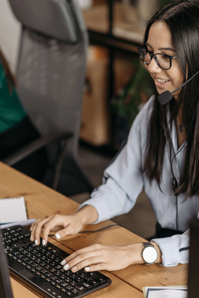 Lady with telephone headset on sitting at a computer.